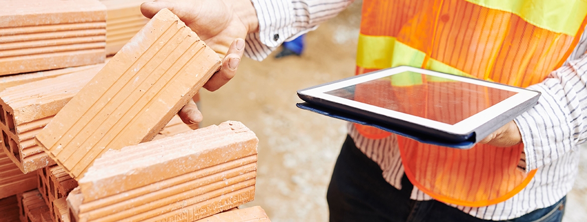 Zdjęcie przedstawia inspektora nadzoru rynku wyrobów budowlanych podczas kontroli na terenie budowy. Na zdjęciu widoczne tylko ręce inspektora. W rękach trzyma tablet.