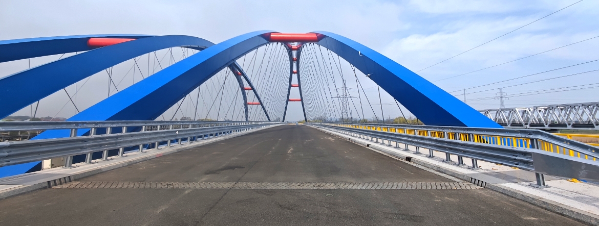 Na zdjęciu pustą drogę na moście i metalowe barierki wyznaczające pasy jezdni.