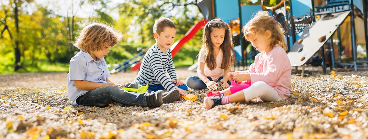Na zdjęciu:Na placu zabaw czworo dzieci bawi się siedząc na piachu. W tle ścianka wspinaczkowa i zjeżdżalnia. 